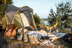 Campsite with tent, trekking shoes, backpack, plaid in the forest